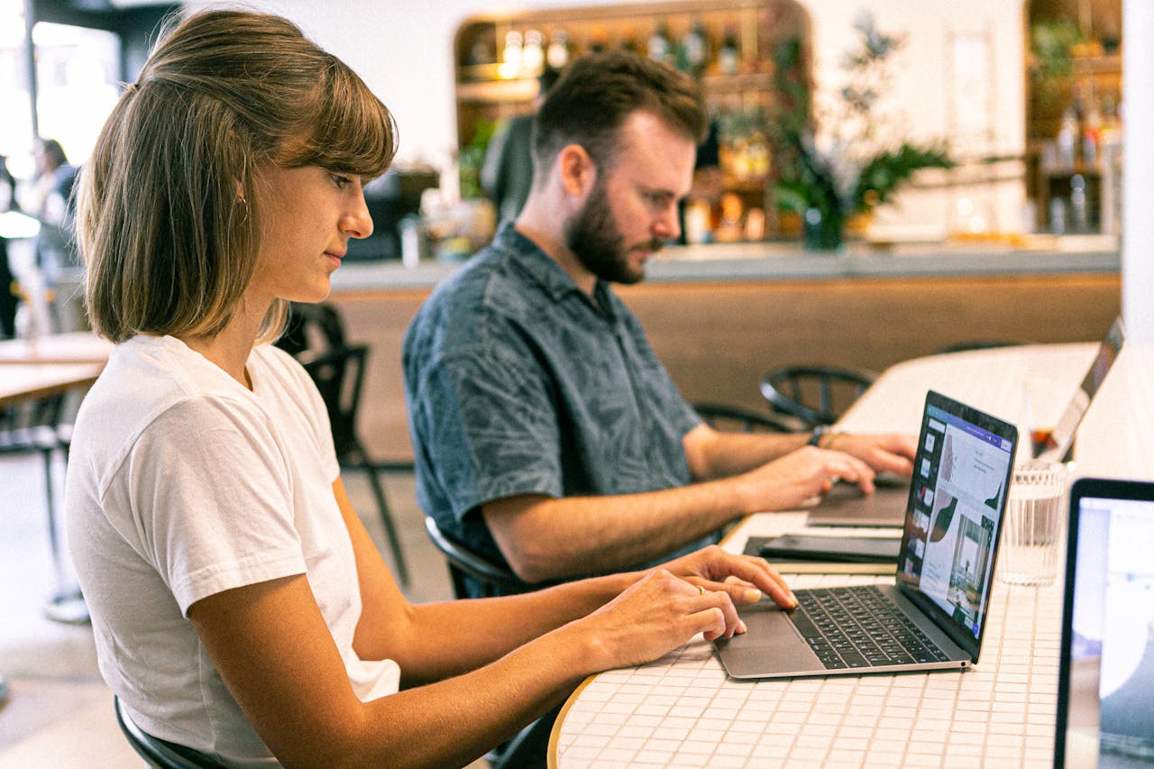 home-hero Two young professionals working on laptops in a modern cafe setting.