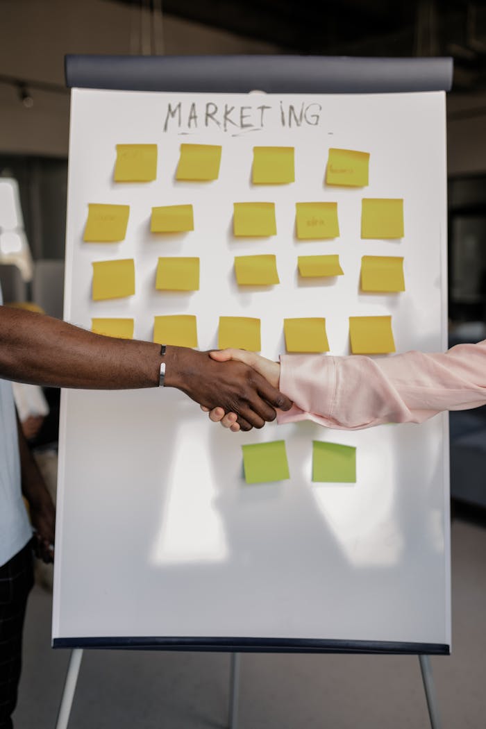 about-us Colleagues shaking hands in front of a marketing board during a business meeting.